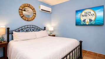 Une chambre à coucher comprenant un lit, un climatiseur fixé au mur, un miroir décoratif, une table de chevet avec une lampe et un tableau encadré représentant un complexe hôtelier.