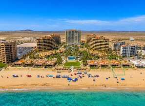 A resort with multiple hotel buildings, a central pool, and a beach area with umbrellas.