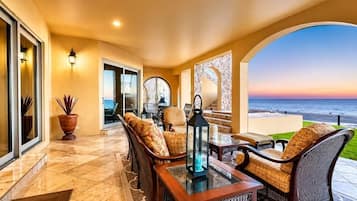 Une terrasse ensoleillée avec des sièges d’extérieur, une vue sur l’océan et une porte vitrée donnant sur l’intérieur.