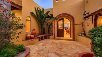A courtyard with stone flooring, a wooden bench, and a door leading to an interior space.