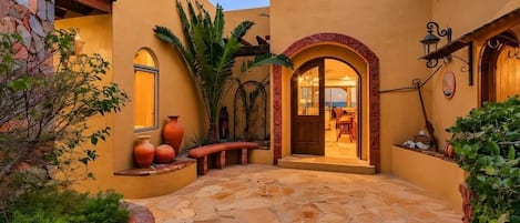A courtyard with stone flooring, a wooden bench, and a door leading to an interior space.
