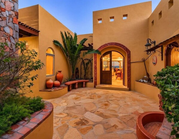 Un patio con piso de piedra, un banco de madera y una puerta que da a un espacio interior.