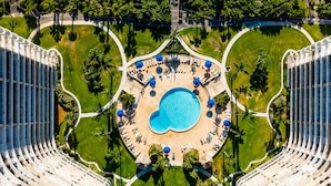 An aerial view of a hotel with a central swimming pool, surrounded by lounge areas and palm trees. - Luxury Beach Resort Marco Island Condo | Ocean Views, Pool & Beach (Marco Island)