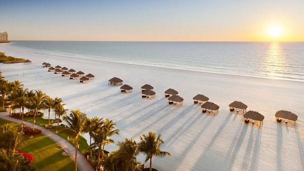 A beach resort with rows of thatched-roof cabanas and palm trees. - Luxury Beach Resort Marco Island Condo | Ocean Views, Pool & Beach (Marco Island)
