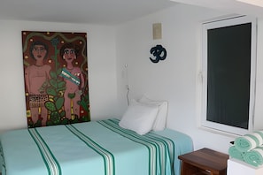 A bedroom with a bed, a painting, a window, and a small table with towels. - Amarilla (San Pedro Pochutla)