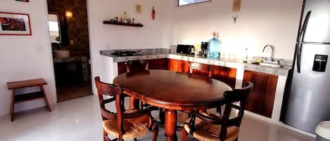 A modern kitchen with a central island, wooden chairs, a built-in refrigerator, and a window above the sink.