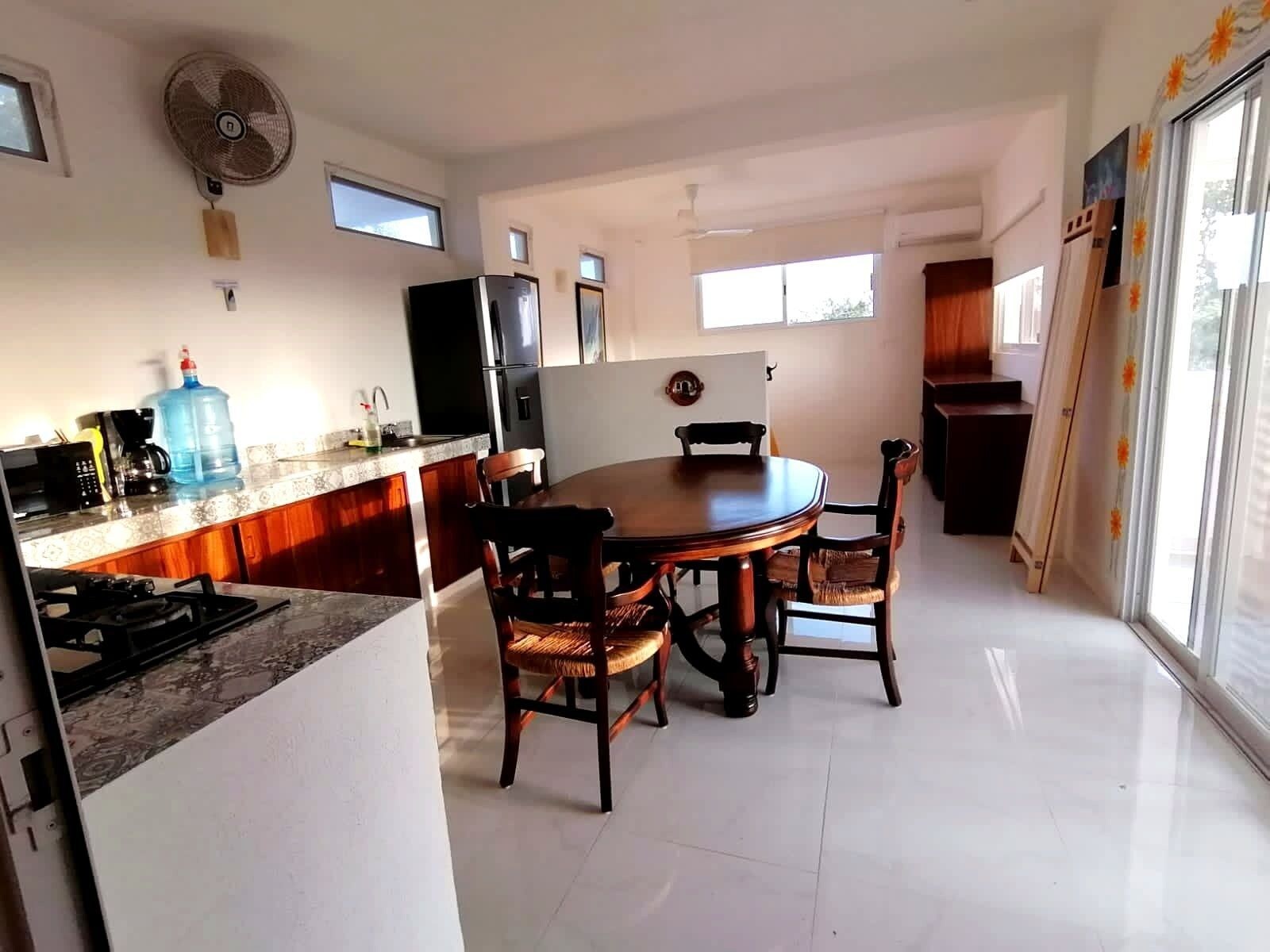 A modern kitchen with a dining table, chairs, a refrigerator, and a large window.