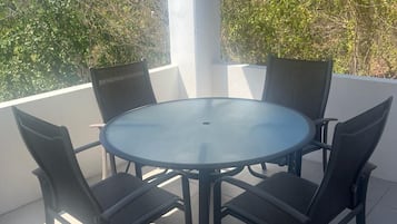 Een ronde glazen tafel met vier stoelen, omgeven door een witte zuil en uitzicht op bomen.
