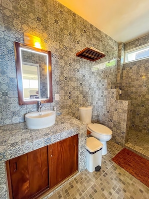 A bathroom with patterned tiles, a sink, a toilet, and a shower area. - Amarilla (San Pedro Pochutla)