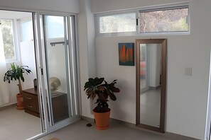 A room with a sliding glass door, a potted plant, a large mirror, and a painting on the wall. - Amarilla Playa Salchi Valentina (San Pedro Pochutla)
