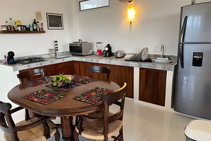 A modern kitchen with a dining table, chairs, a refrigerator, and a microwave. - Amarilla (San Pedro Pochutla)