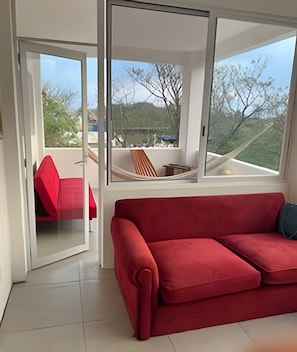 Un sofá rojo en una habitación moderna con ventanas amplias, una silla roja y una hamaca.
