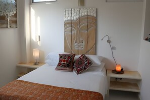 A bedroom with a bed, pillows, a nightstand with a lamp, a wall art piece, and a bedside table with a candle. - Amarilla Playa Salchi Valentina (San Pedro Pochutla)
