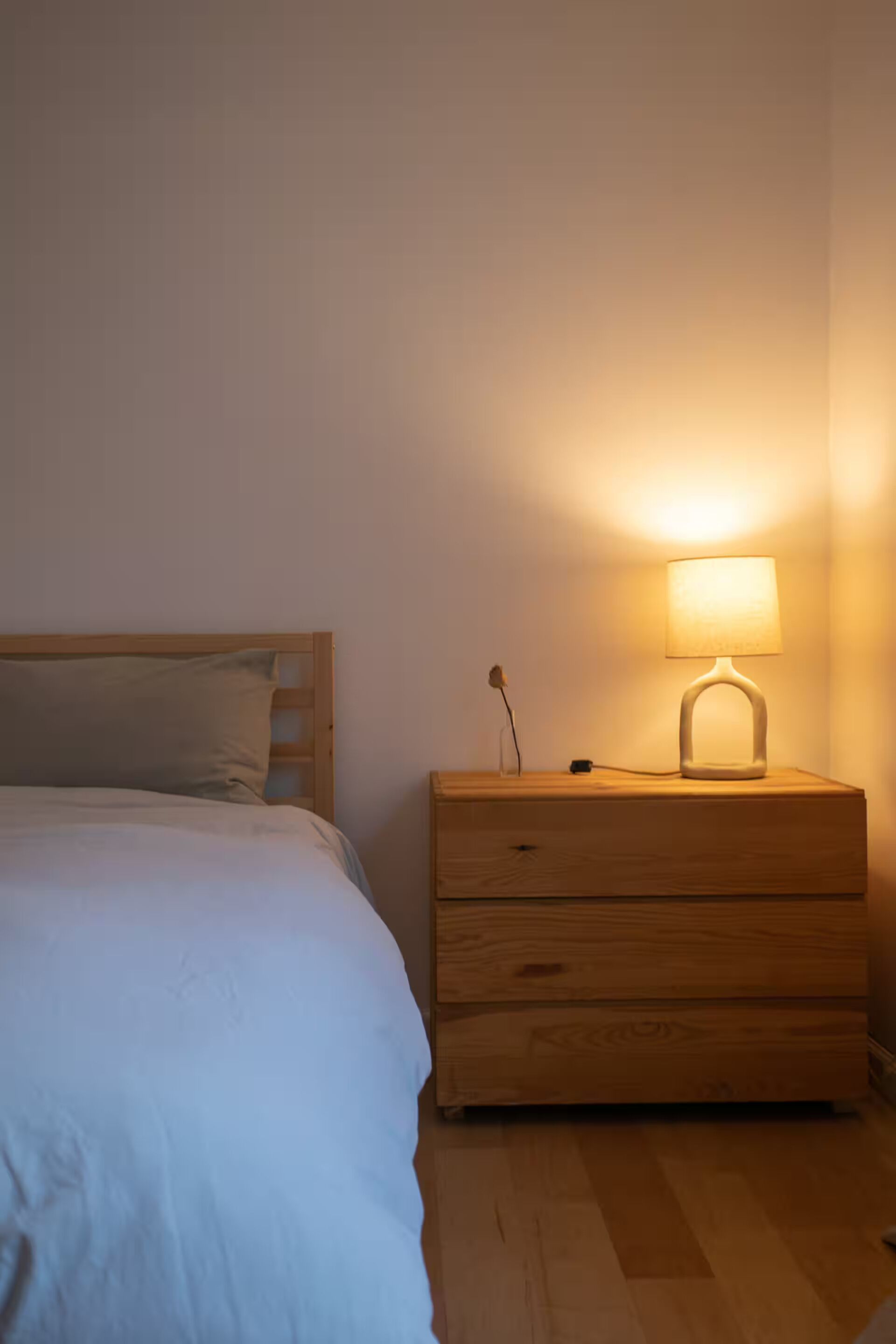 A bedroom with a bed, a bedside table with a lamp, and a wooden nightstand.