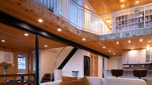 Un vaste espace de vie doté d’un plafond en bois, d’un canapé blanc, d’une table ronde en bois et d’un escalier menant à un niveau supérieur.