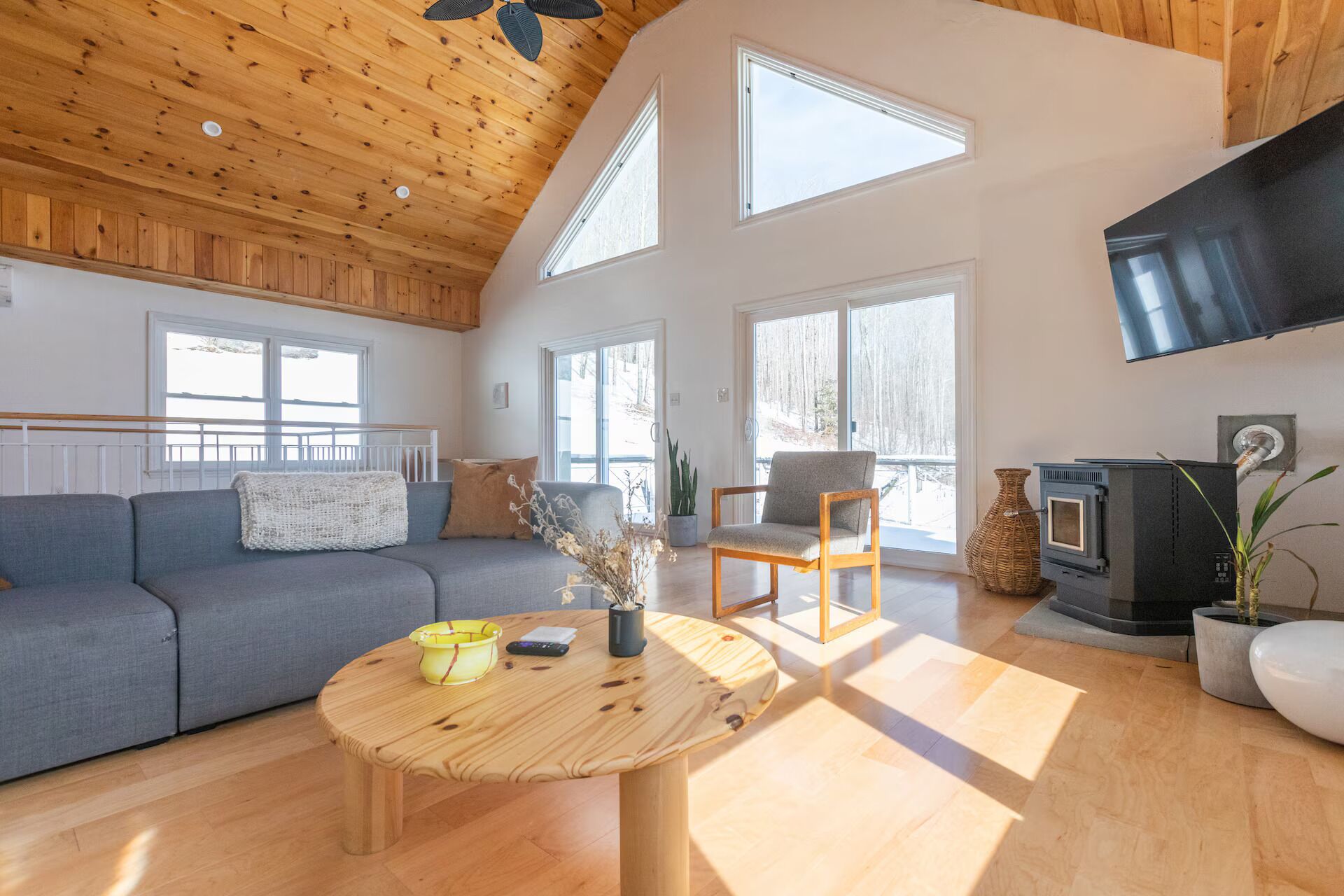 A spacious living room with a wooden ceiling, a sofa, a chair, a round wooden coffee table, and a fireplace.