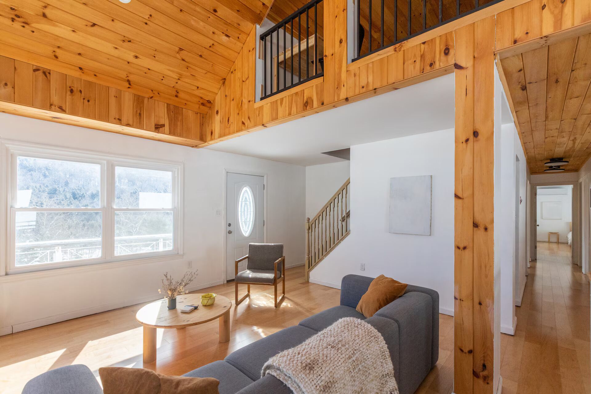 A spacious loft with a high ceiling, wooden beams, a staircase, and a large window.