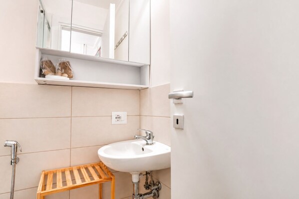 Une salle de bain avec un lavabo blanc, une étagère en bois, un miroir et une douche.