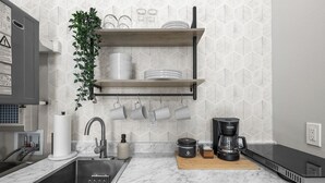 Una cocina con un lavamanos, una cafetera y una repisa con vajilla.