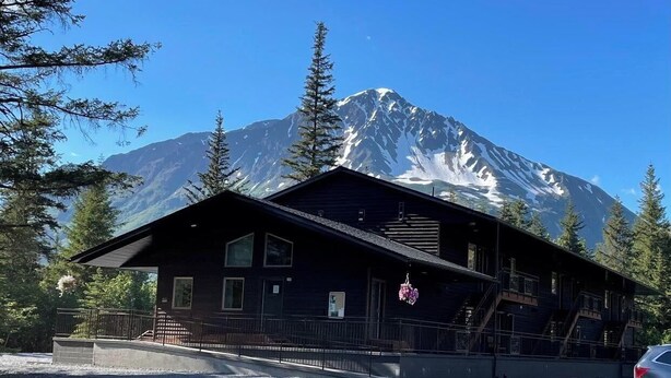 Un chalet doté d’une grande véranda, d’un escalier et surplombant un paysage montagneux.