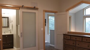 A bedroom with a bed, a dresser, a mirror, a door, and a window.