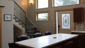 A dining area with a table, chairs, a staircase, and a view through a window.
