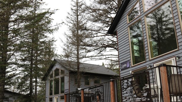 A two-story house with large windows, a wooden deck, and a metal railing.