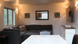 A living room with a sectional sofa, a dining table, and a kitchen area with cabinets and a countertop.