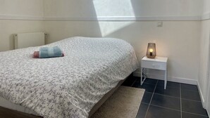 Een slaapkamer met een bed, nachtkastje, lamp en een raam dat een schaduw werpt.