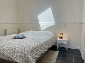 Ein Schlafzimmer mit einem Bett, einem Nachttisch, einer Lampe und einem Fenster, das einen Schatten wirft.