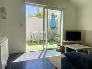 A living room with a TV, sofa, and a sliding glass door leading to a patio. - Proche port et plage des Minimes (LA ROCHELLE)