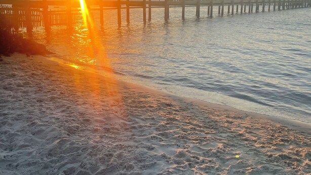 A pier extending into calm waters with a sunset in the background.