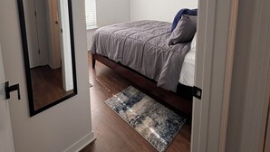 A bedroom with a bed, a ceiling fan, a window with blinds, a painting on the wall, and a rug on the floor.
