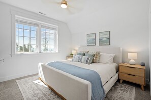 Ein Schlafzimmer mit einem großen Bett, zwei Nachttischen, einem Fenster mit Jalousien und zwei Wandbildern.