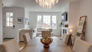Un comedor con una mesa de madera, sillas, una araña y vistas al exterior.