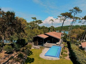 Eine Holzhütte mit Schwimmbecken, umgeben von Bäumen und blauem Himmel.