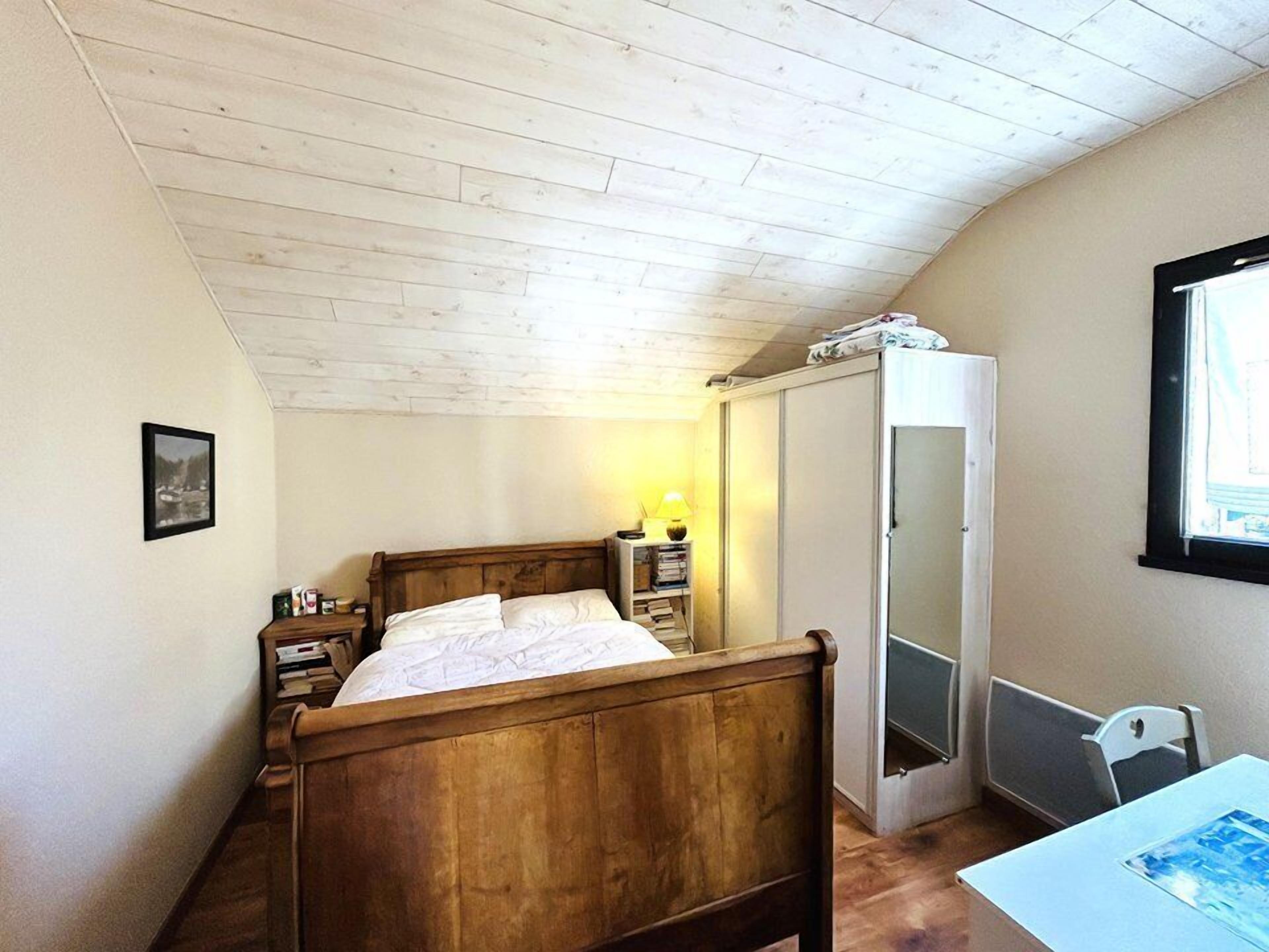 Un dormitorio con una cama de madera, una mesita de noche con lámpara, un armario y una ventana.