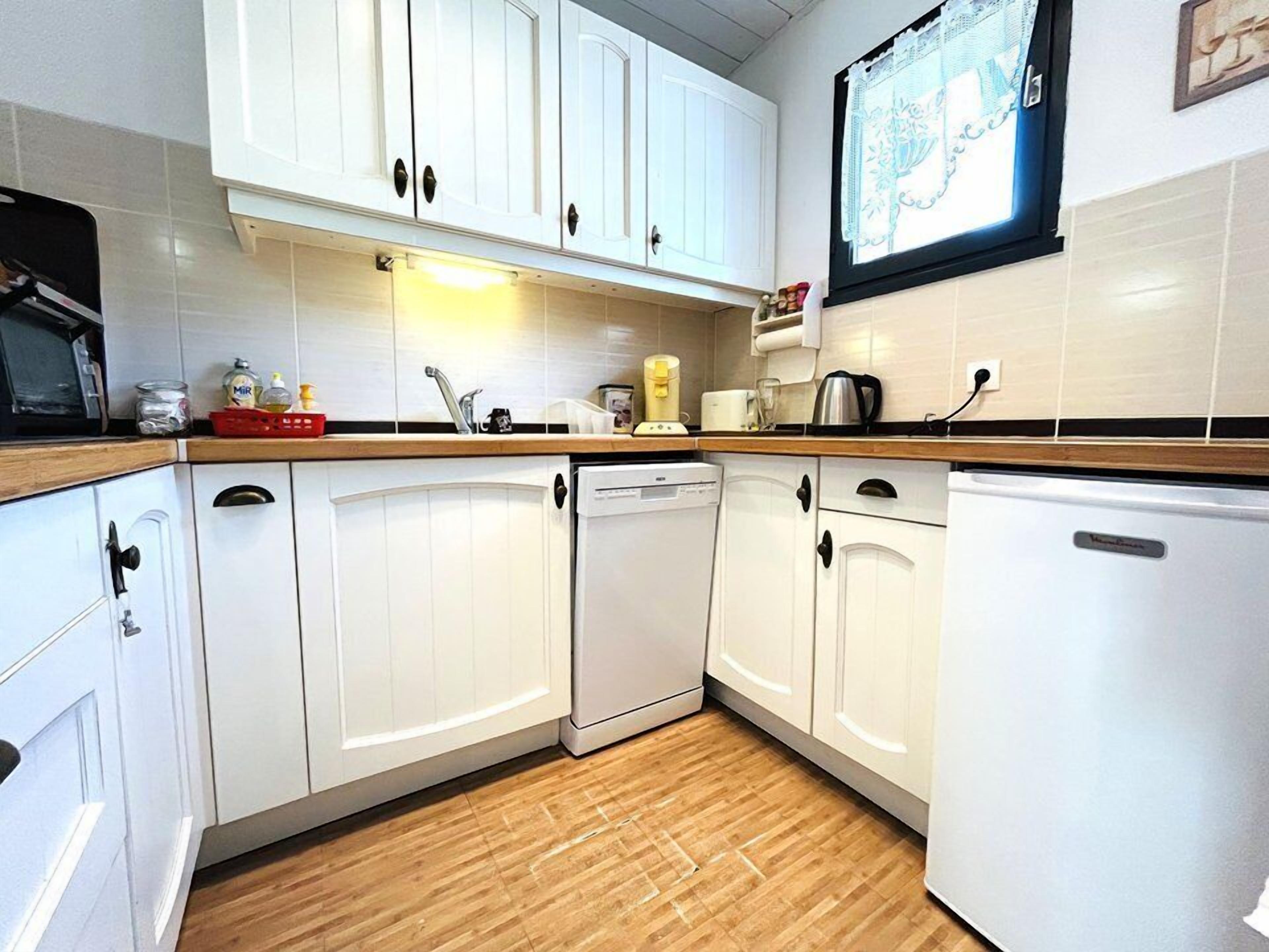 A kitchen with white cabinets, a dishwasher, a refrigerator, and a window with a view.