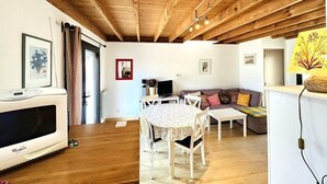 Un accogliente soggiorno con travi in legno, una zona pranzo con tavolo e sedie, un divano e un televisore.
