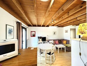 A cozy living room with wooden beams, a dining area with a table and chairs, a sofa, and a television. - House 3 bedrooms 4 people in Guidel, only 400 m from the beach, enclosed garden, wifi (GUIDEL)