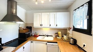 Una cucina compatta con mobili bianchi, una cappa in acciaio inossidabile, un lavello a due vasche e una finestra con tende in pizzo.