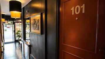 Een hotelentree met een donkere muur, een houten deur met daarop '101', een zwarte mat en een ingelijst schilderij.