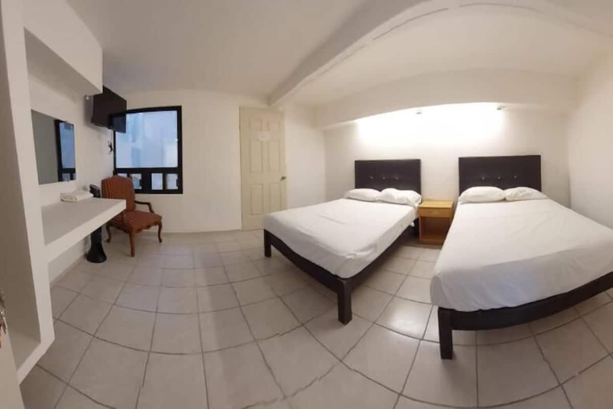 Un dormitorio con dos camas, un escritorio, una silla, un televisor y una ventana.