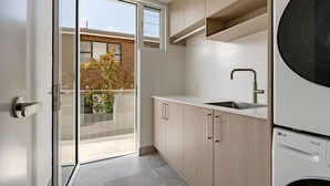 Een moderne keuken met een ingebouwde wasmachine, schuiframen naar een balkon en uitzicht op een bakstenen gebouw.