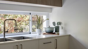 Een keuken met een raam, een spoelbak, een plant in een pot en keukengerei op het aanrecht.
