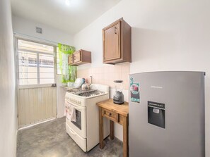 A compact kitchen with a stove, a refrigerator, a wooden table, and a window with curtains.