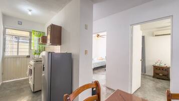 A compact kitchen with a refrigerator, stove, and cabinets, leading to a bedroom with a bed and a dresser.