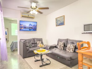 A living room with two grey sofas, a small table with a vase, a ceiling fan, and a painting on the wall. - Casa equipada 3 recs. cerca aeropuerto (Ciudad Apodaca)
