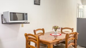 Spiseområde med et træbord, fire stole, en lille vase med blomster, en mikrobølgeovn på en hylde og et køleskab.