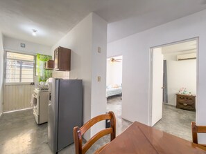 Une cuisine compacte équipée d’un réfrigérateur, d’une cuisinière et de placards, qui donne sur une chambre avec un lit et une commode.